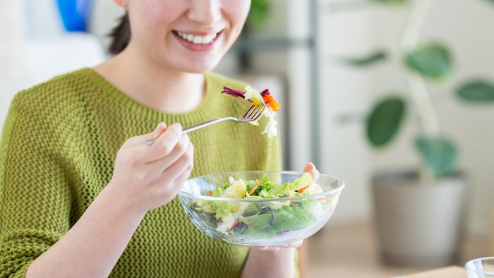 Eine Frau isst Salat aus einer Glasschale.