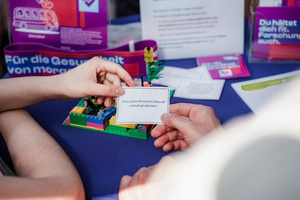 Zwei Hände von zwei verschiedenen Personen halten einen Zettel in die Kamera. Darauf steht: Was sollte Medizin in Zukunft unbedingt können?