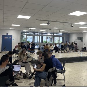 Junge Menschen sitzen in Kleingruppen in einem Schulflur zusammen.