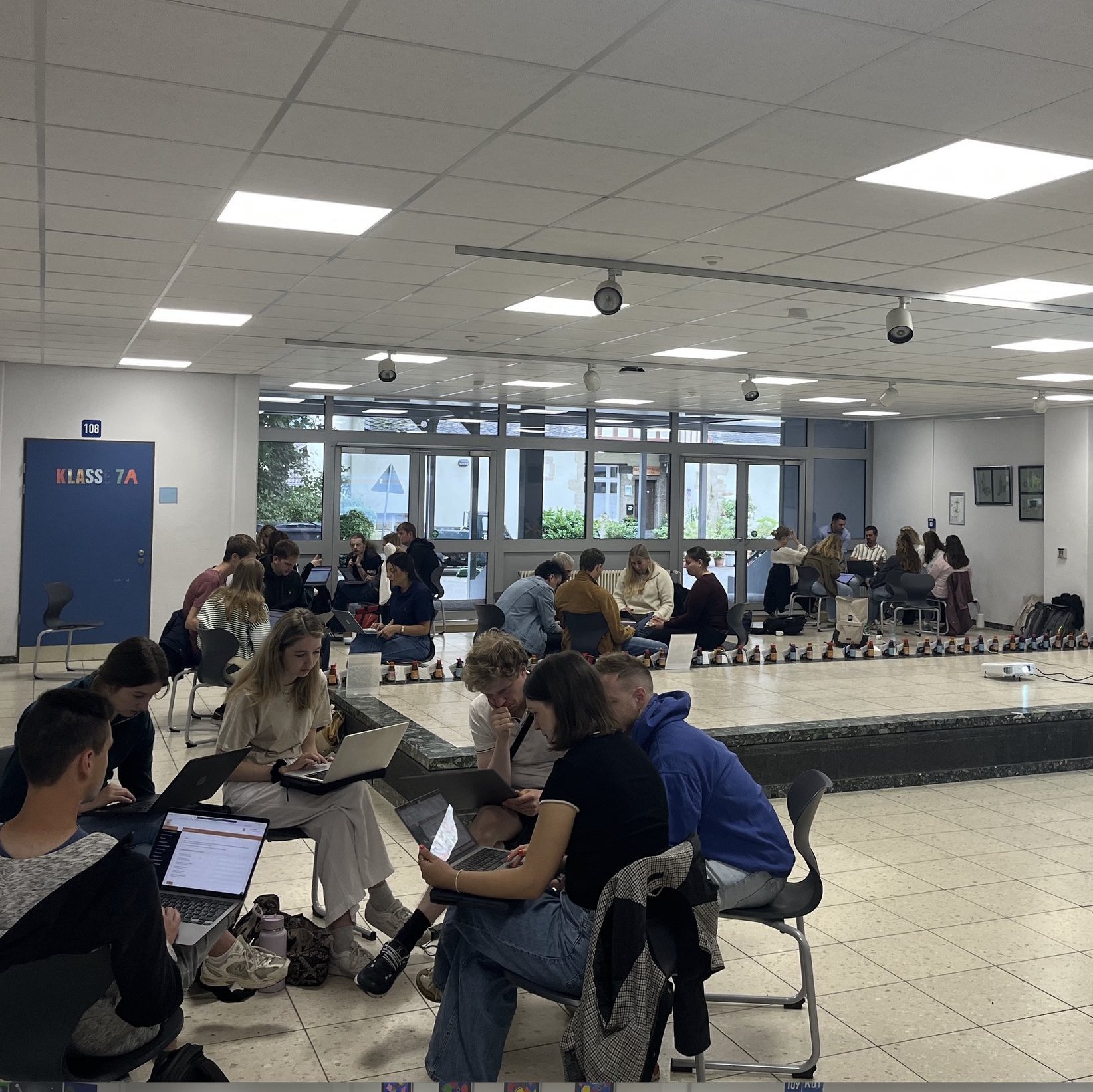 Junge Menschen sitzen in Kleingruppen in einem Schulflur zusammen.