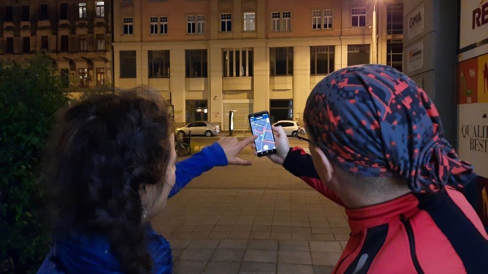 Ein Mann und eine Frau stehen bei Nacht vor einem Haus mit einer Straßenlaterne. Sie stehen mit dem Rücken zur Kamera und halten ein Handy mit der Nachtlicht-App in der Hand. 