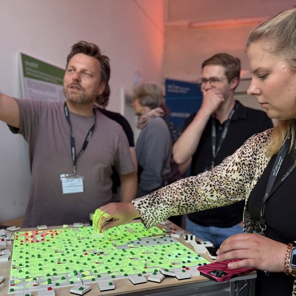 Mehrere Personen tauschen sich vor einem Lego-Windpark-Modell aus und gestikulieren dabei lebhaft.