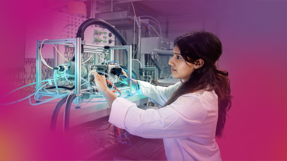 Frau im weißen Kittel arbeitet an einer technischen Apparatur, aus der Schläuche herausragen