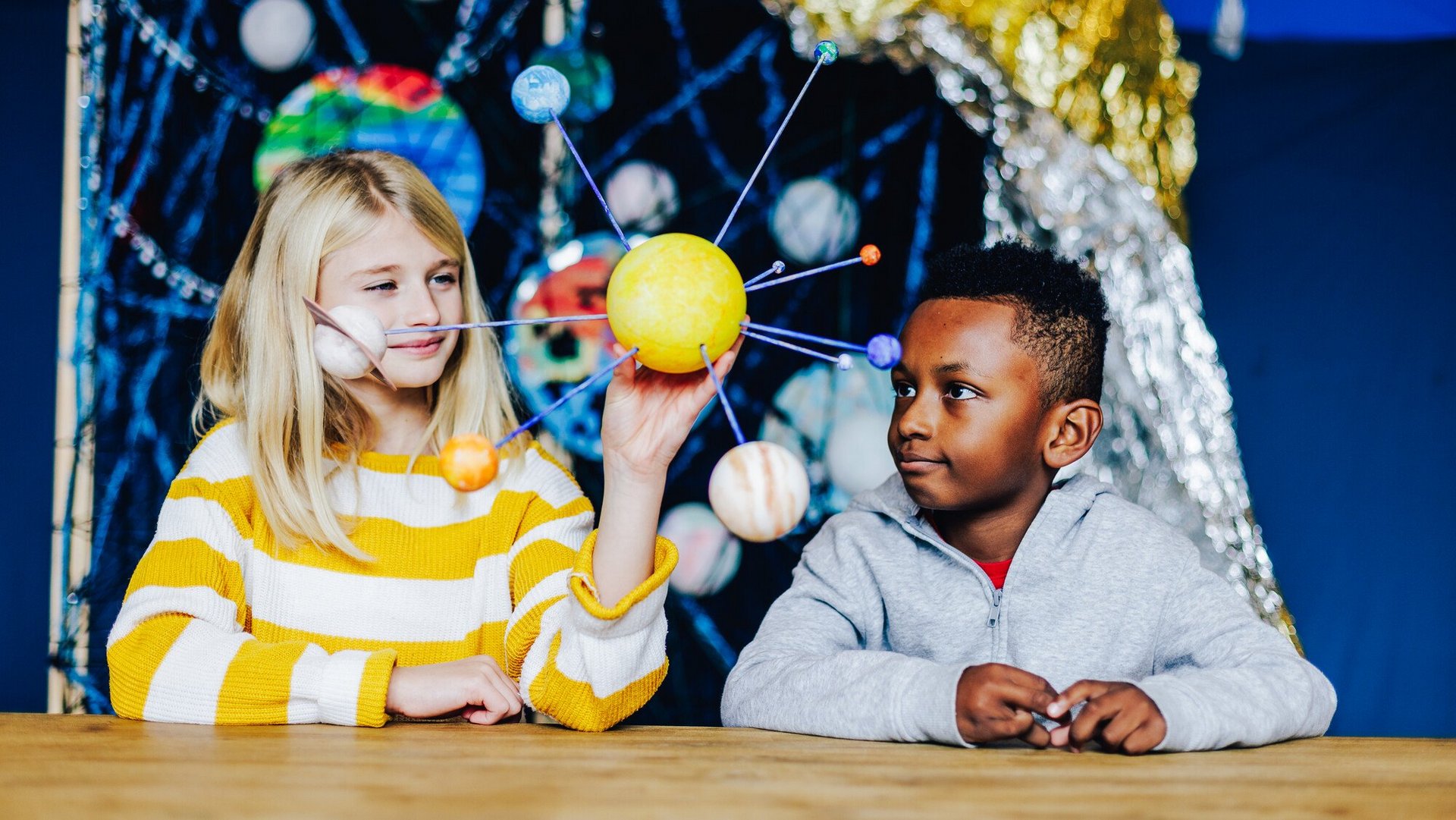 Zwei Kinder halten ein illustriertes Sonnensystem in der Hand.