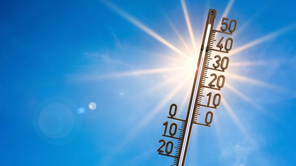 Thermometer mit blauem Himmel und Sonne im Hintergrund