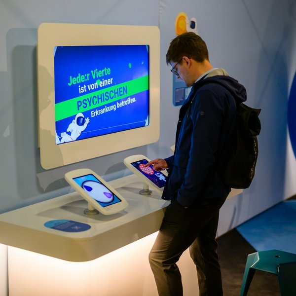 Ein Mann spielt an einem Tablet-Computer an einem der Exponate zu psychischer Gesundheit.