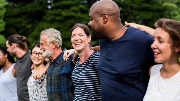 Eine vielfältige Gruppe Menschen steht Arm in Arm im Freien.