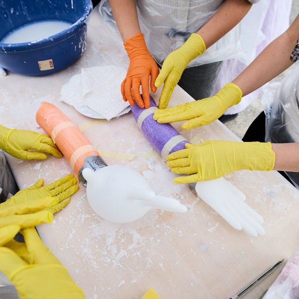 Kinderhände mit Gummihandschuhen, die auf einem Tisch liegende bunte Rollen mit aufgeblasenen Gummihandschuhen an einem Hände berühren.