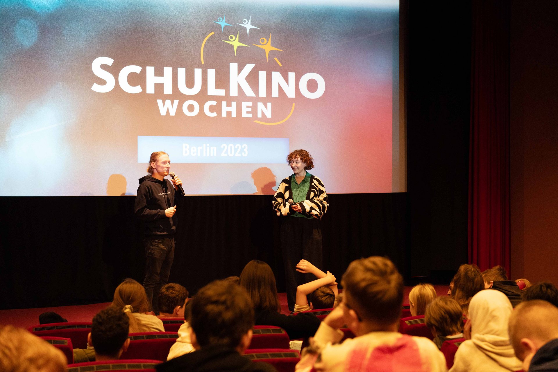 Zwei Menschen sprechen vor einem Publikum im Kino.