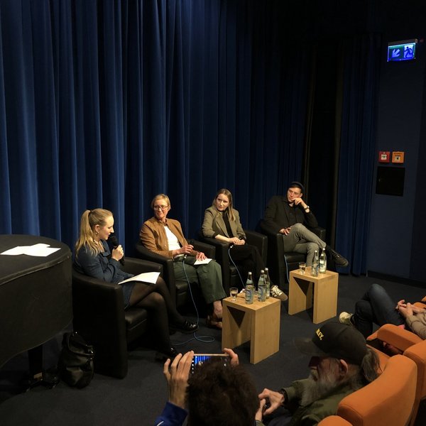 Vier Personen sitzen in einem Kinosaal vor Publikum, eine Moderatorin spricht in ein Mikrofon.