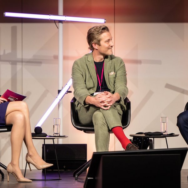 Drei Personen sitzen auf Stühlen auf einer Bühne, Bundesminister für Bildung und Forschung Cem Özdemir spricht in ein Mikrofon.