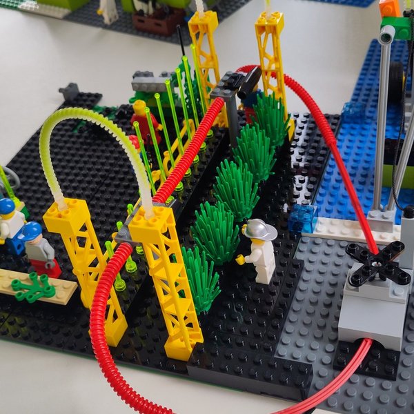 Modell aus Klemmbausteinen mit Pflanzen, Schläuchen und Figuren auf einem Tisch