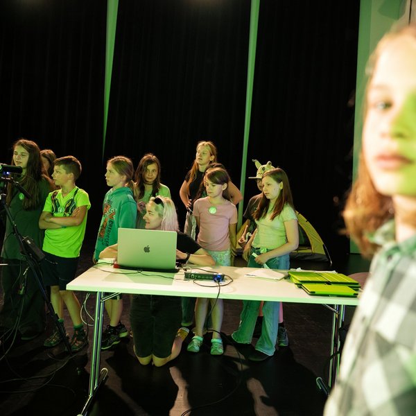 Schülerinnen und Schüler beobachten eine Aufzeichnung vorm Greenscreen.