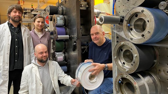 Wissenschaftler an einer Rollendruckmaschine mit dem Testdruck einer leitfähigen Solarzellen-Schicht.