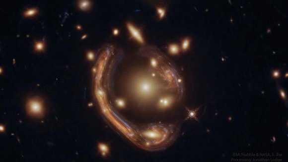 Zwei zu Kreissegmenten verzerrte Abbilder einer Galaxie, umgeben von hellen Flecken auf schwarzem Hintergrund. 