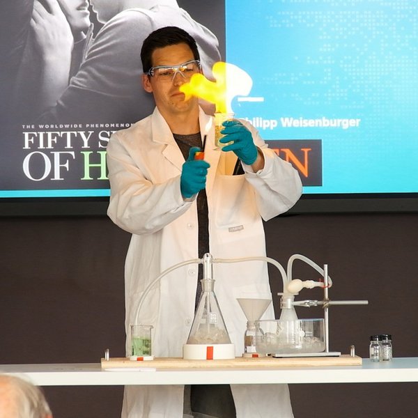 Philipp Weisenburger mit Schutzbrille und Kittel entzündet eine Flamme mit Wasserstoff.