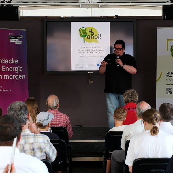 Moderator Martin Stammberger mit Mikrofon vor Publikum.