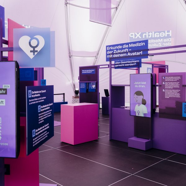 Innenraum einer Ausstellung mit verschiedenen Bildschirmen und Tafeln, zu lesen ist die Überschrift "Erkunde die Medizin der Zukunft – mit deinem Avatar!"