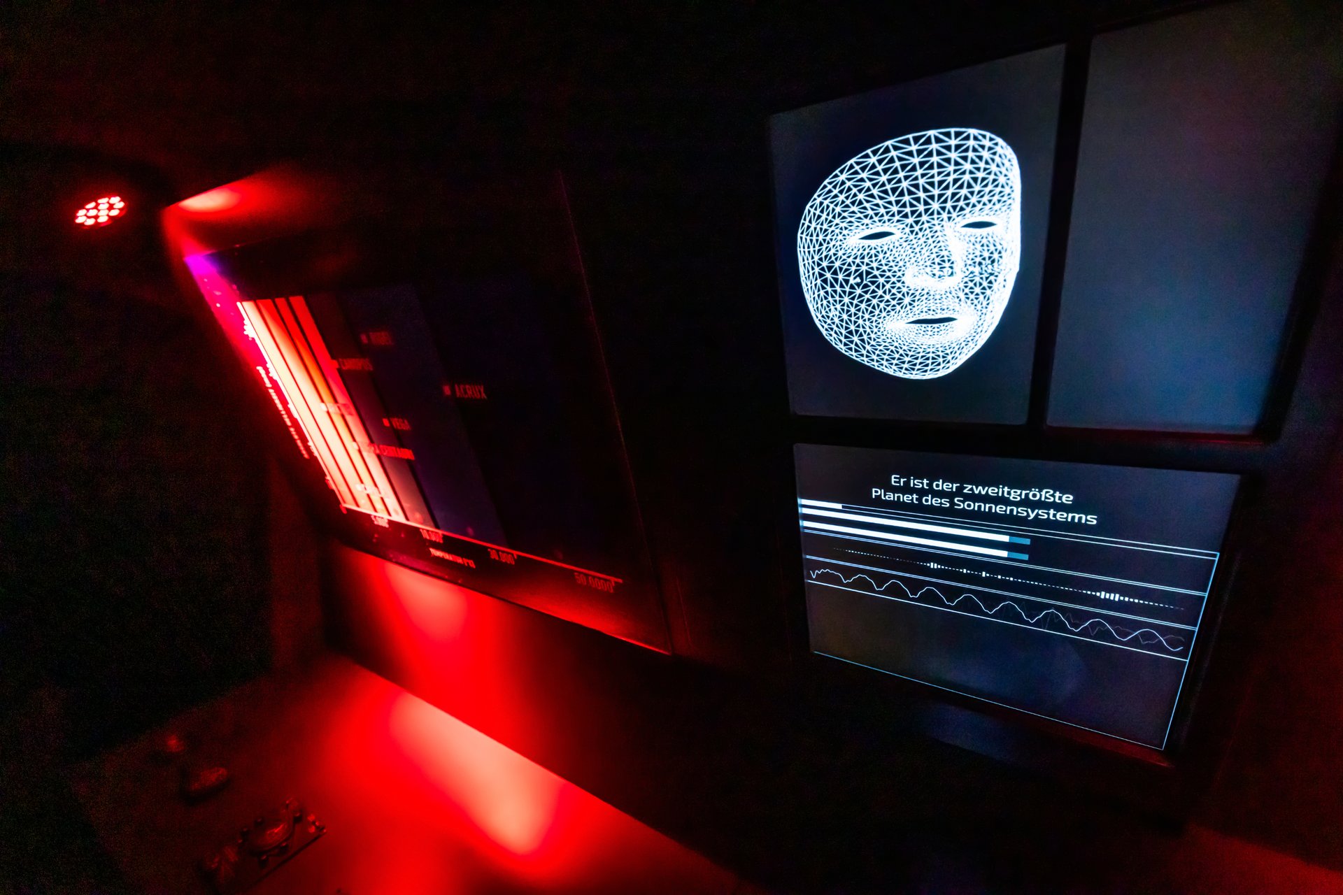 Ein Display zeigt eine weiße Maske, der Raum ist dunkel und nur links rot beleuchtet.