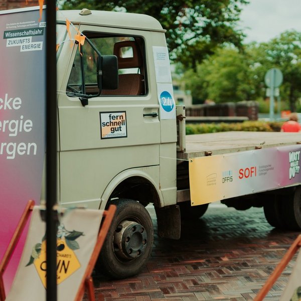 LKW mit leerer Ladefläche, davor ein Roll-up mit der Aufschrift "Entdecke die Energie von morgen".