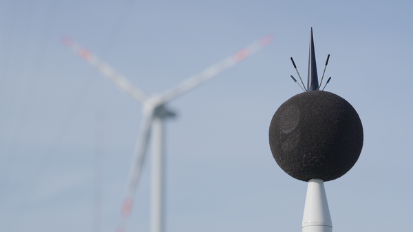 Ein Mikrofon vor einer Windkraftanlage.