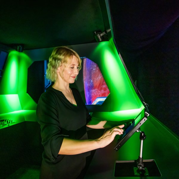 Eine Frau steht an einem kleinen Bildschirm in einem grün erleuchteten Raum