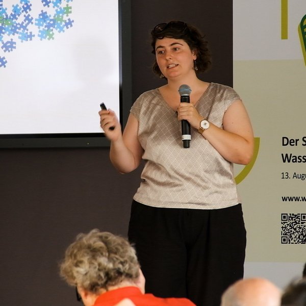 Michaela Löffler mit einem Mikrofon in der Hand vor Publikum.