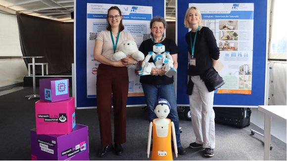 Gruppenfoto des Projektteams. Mittige Person hält einen kleinen Roboter in den Händen, vor der Personengruppe ist ein weiterer kleiner Roboter platziert.